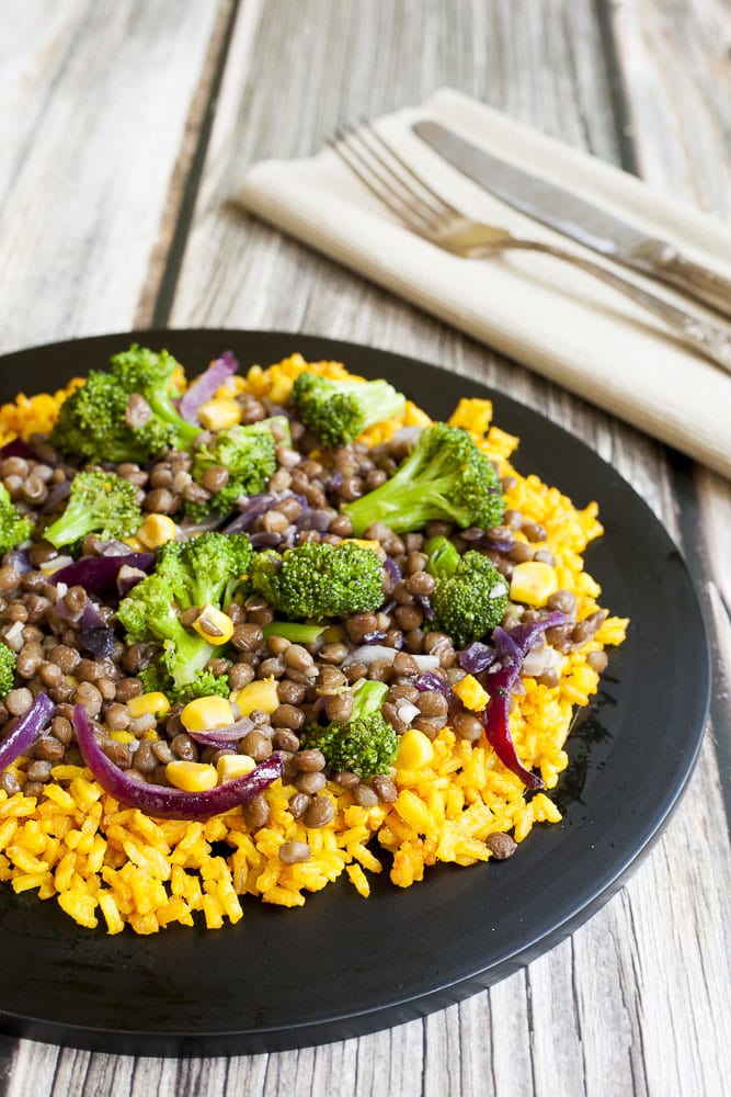 Broccoli Lentil Stir Fry served with turmeric rice on a black plate with silver fork and knife
