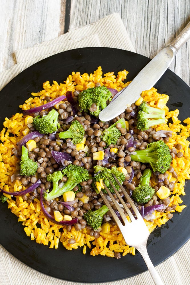 Broccoli Lentil Stir Fry served on turmeric rice in a black plate with silver fork and knife