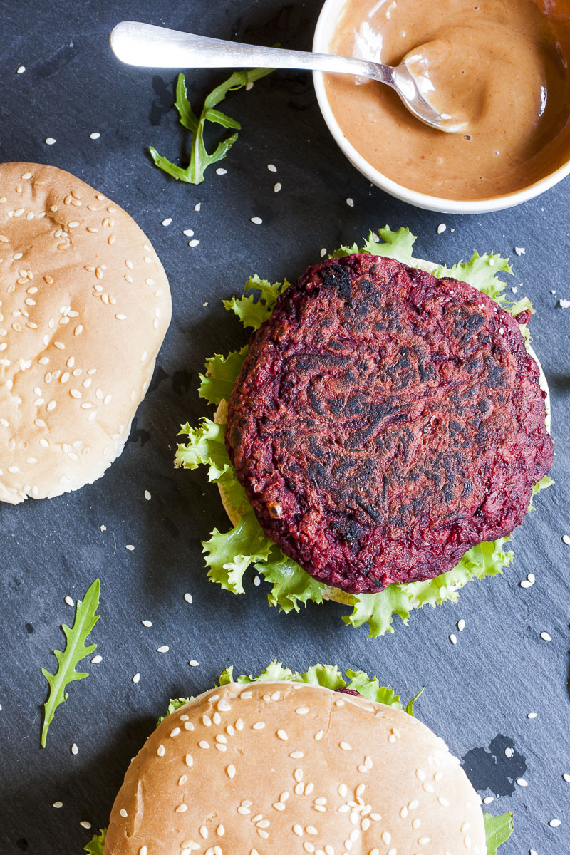 Purple burger patty from above on a black slate board. Toasted buns are next to it. 