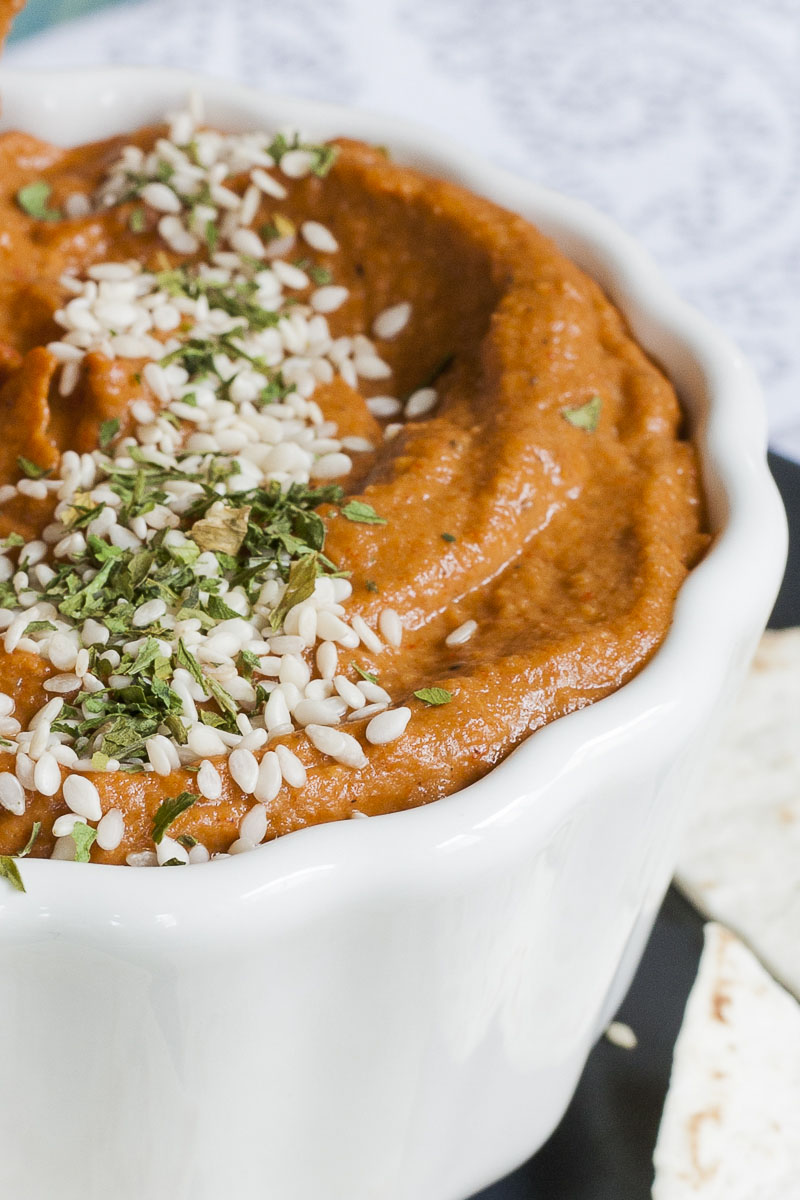 Orange brownish cream in a white bowl sprinkled with green dried herbs and tiny white seeds