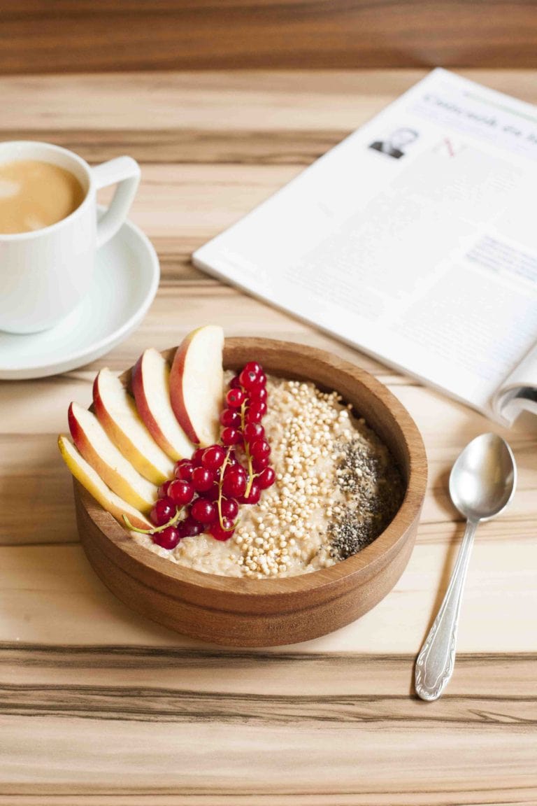 Bowl of Vegan Apple Cinnamon Oatmeal made on stove top - topped with apple slices, red currant, chia seeds and puffed quinoa