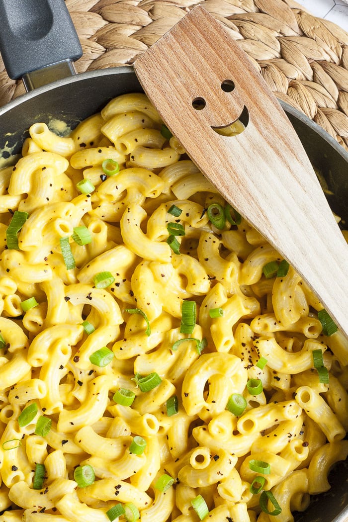 A frying pan with paste and yellow sauce topped with chili flakes and chopped green onion. A wooden smiling spatula is place next to it. 