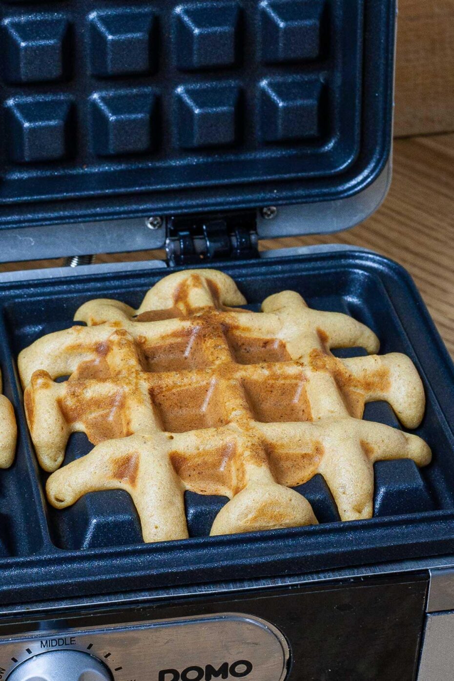 A waffle iron with yellow cooked batter with a lid open.