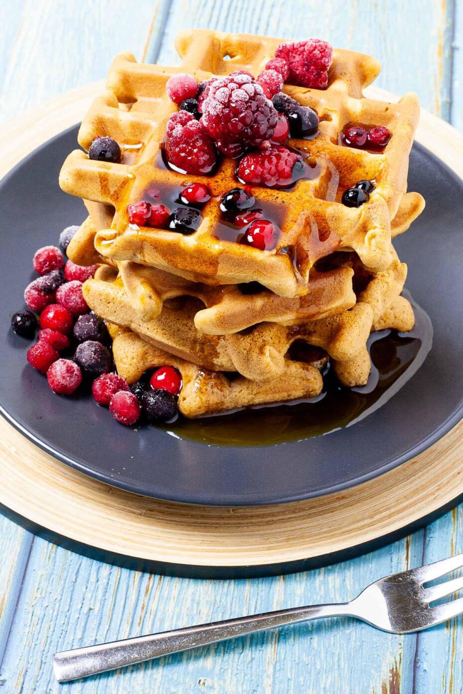 Black plate with a stack of waffles topped with mixed berries and maple syrup