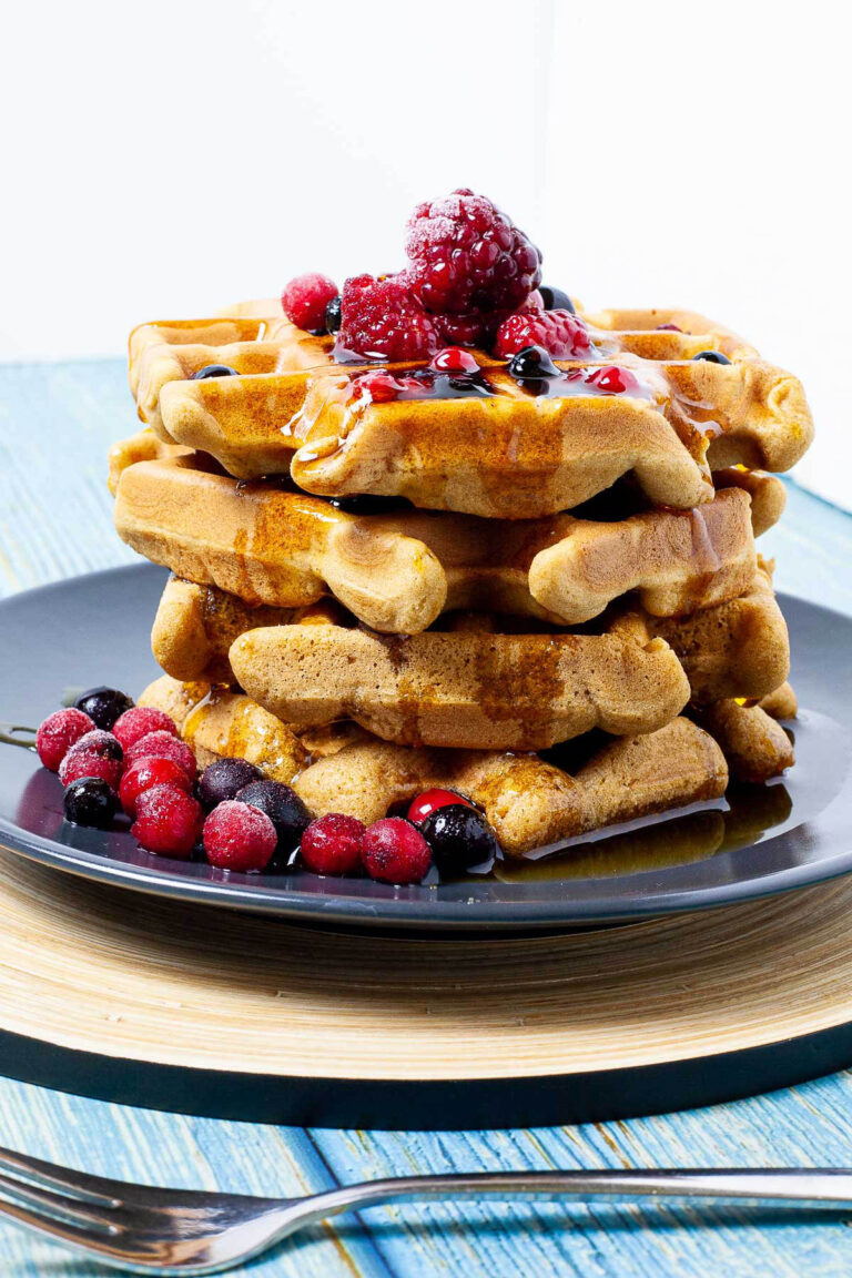 Black plate with a stack of waffles topped with mixed berries and maple syrup