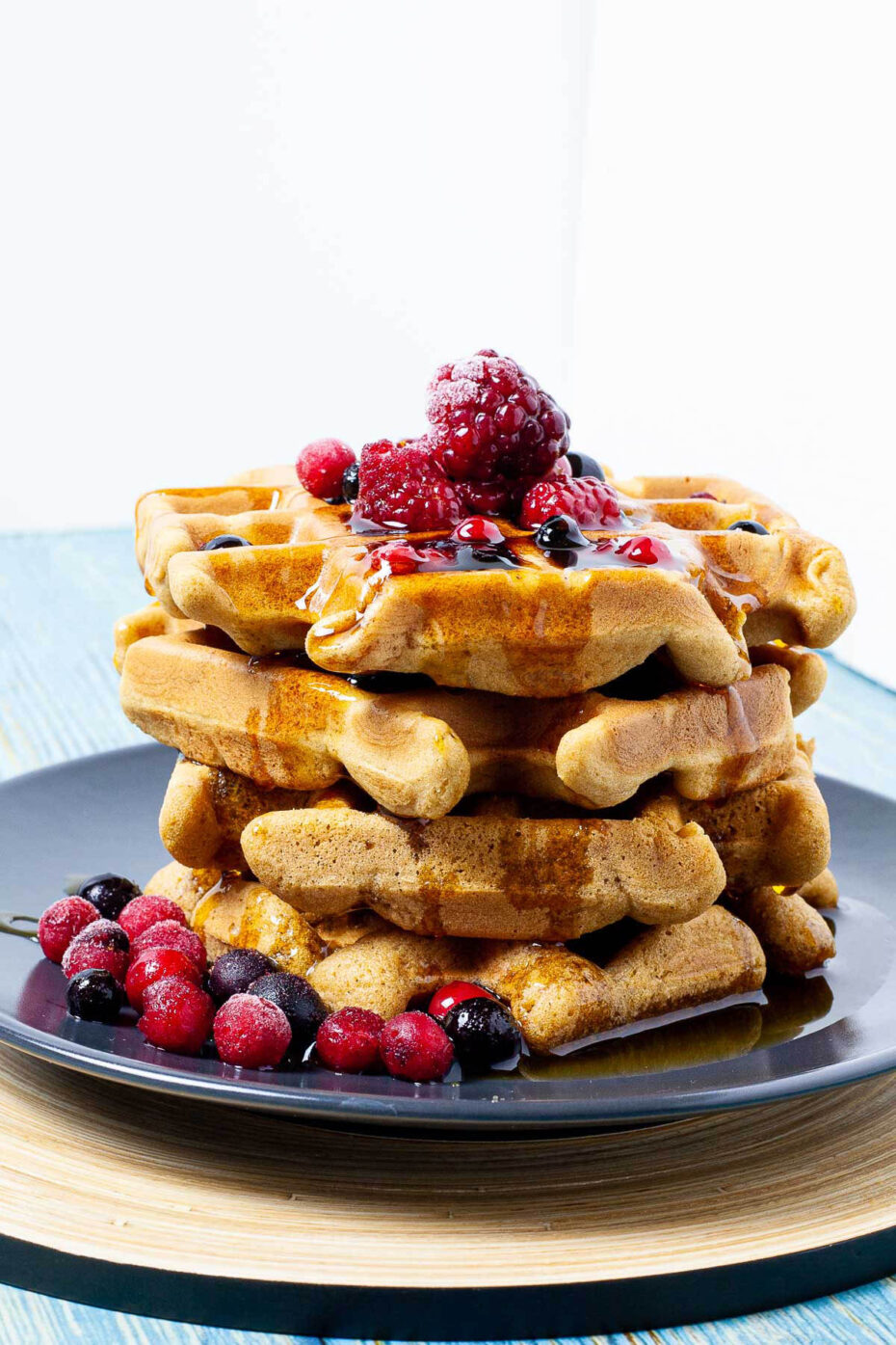 Black plate with a stack of waffles topped with mixed berries and maple syrup
