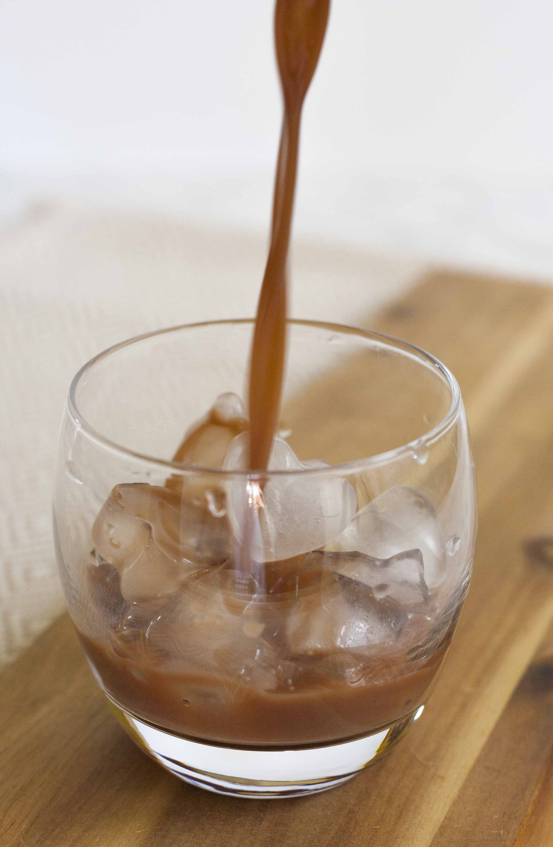 Someone is pouring brown creamy drink into a whiskey glass with heart-shaped ice. 