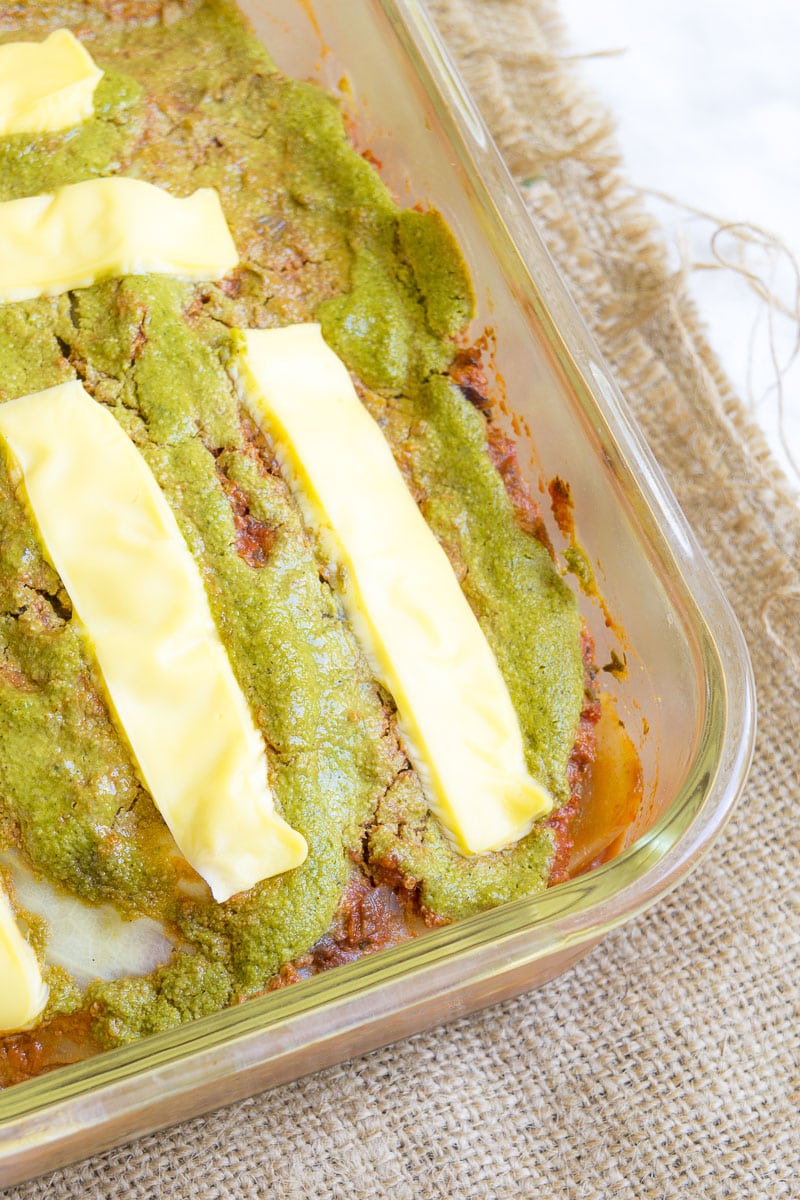 Close-up of the pan full of cabbage lasagna. You can see the top cheese layer and the green spinach alfredo below.