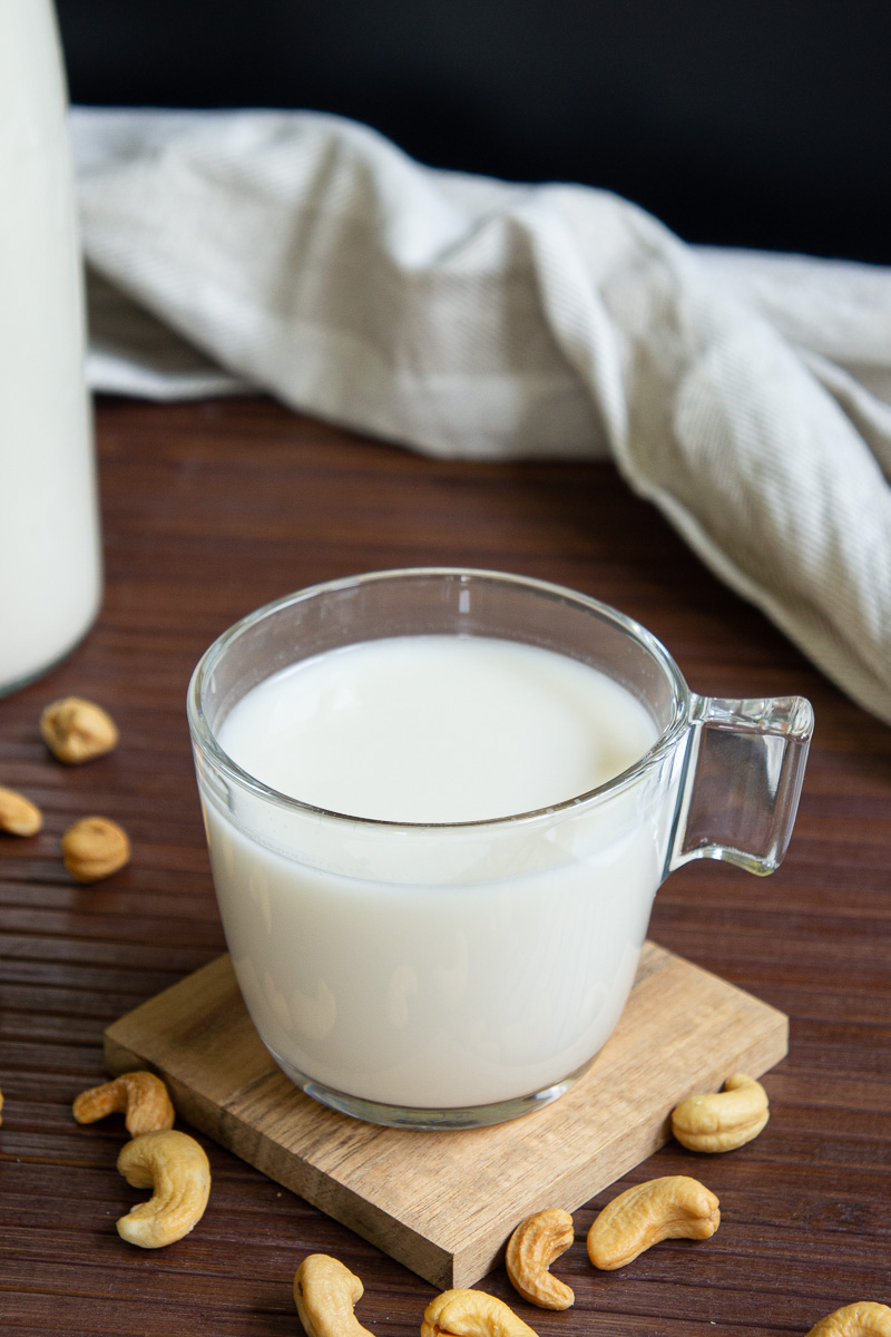 Glass of cashew milk on a wooden coaster. Cashews around.