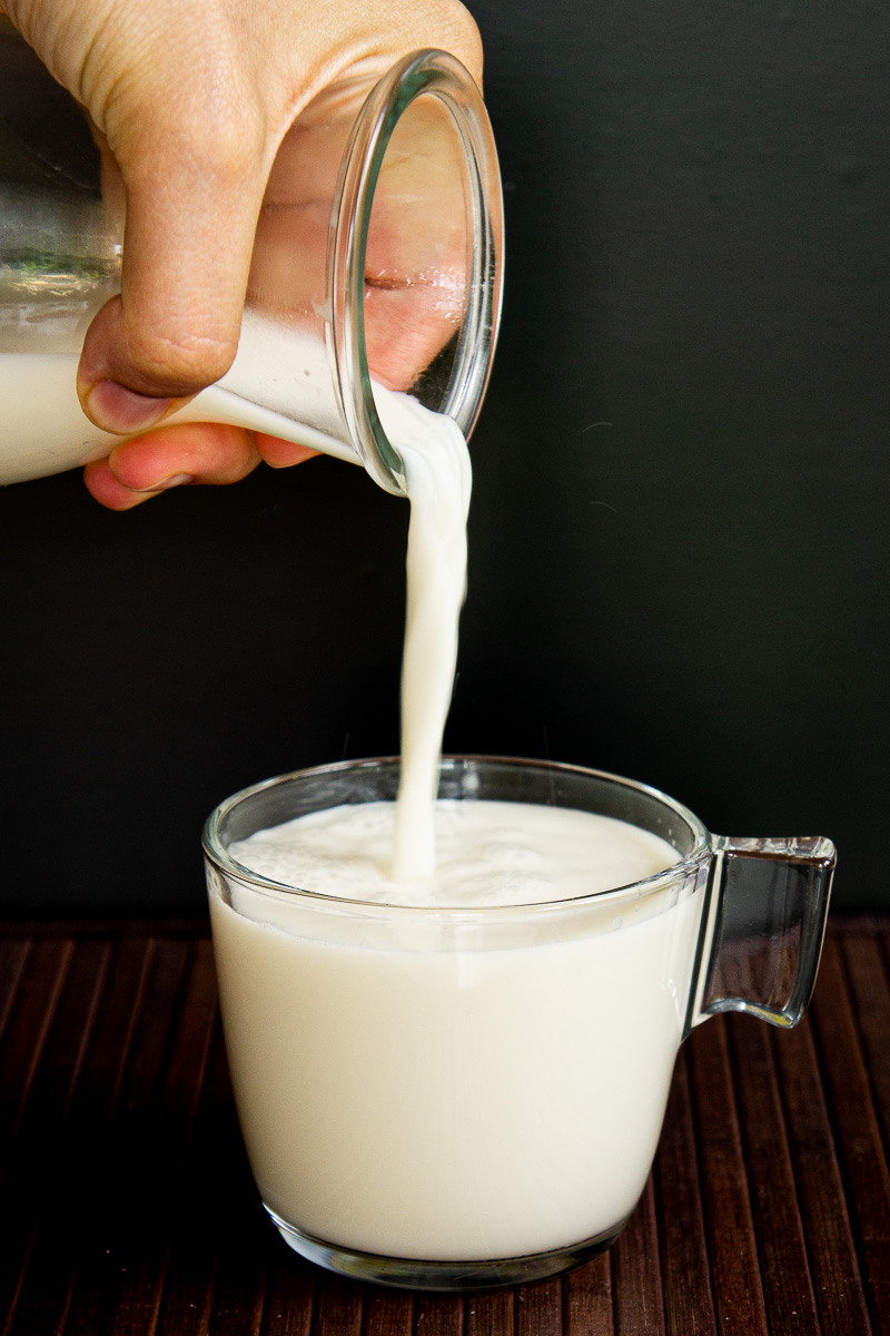 Pouring cashew milk from a glass jar to a glass mug