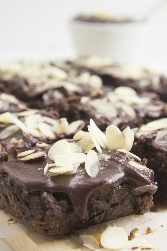 Close-up of vegan sweet potato brownies with chocolate frosting and sliced almonds cut into squares.