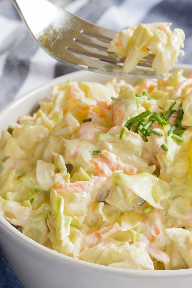 White bowl of shredded cabbage and carrots in a creamy sauce. A fork is taking a bite. 