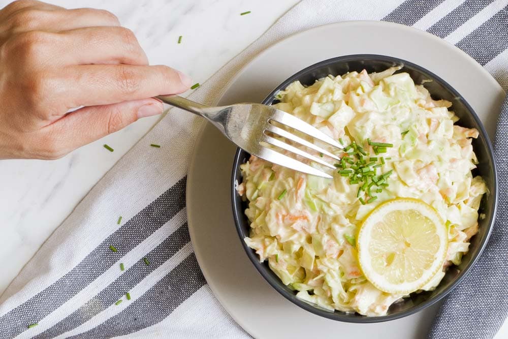 Black bowl of shredded cabbage and carrots in a creamy sauce. A fork is taking a bite.