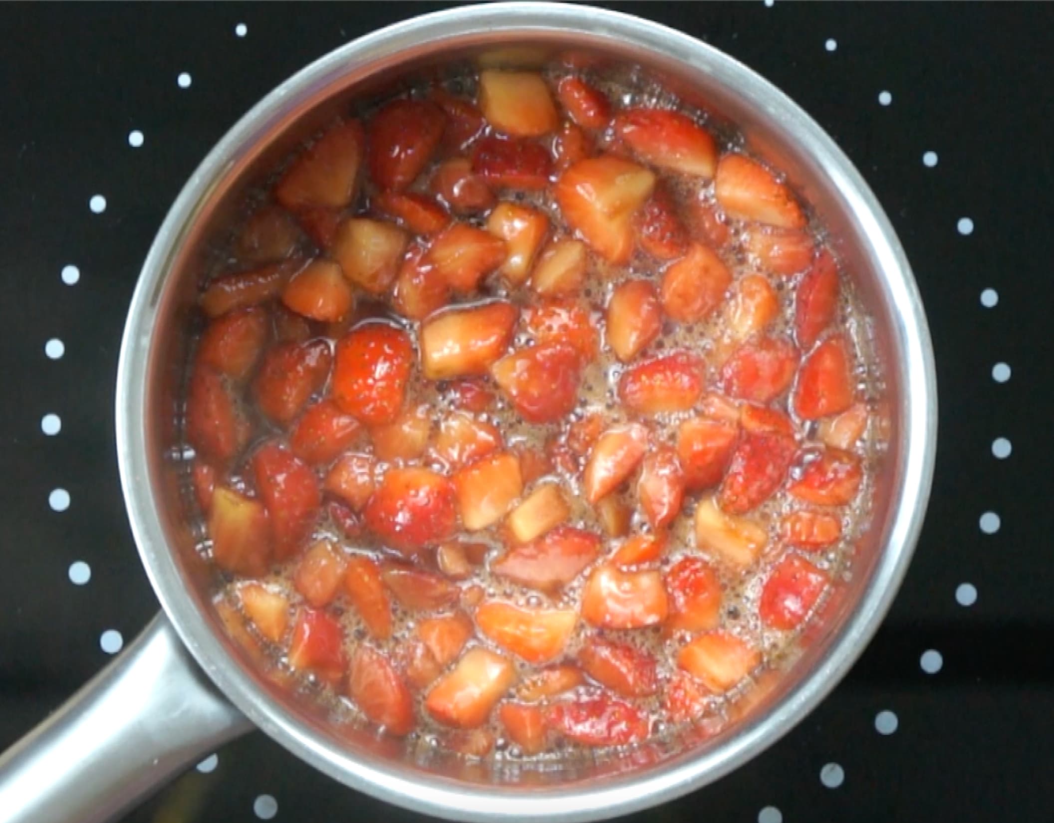Strawberry pieces in a small saucepan with bubbling water.