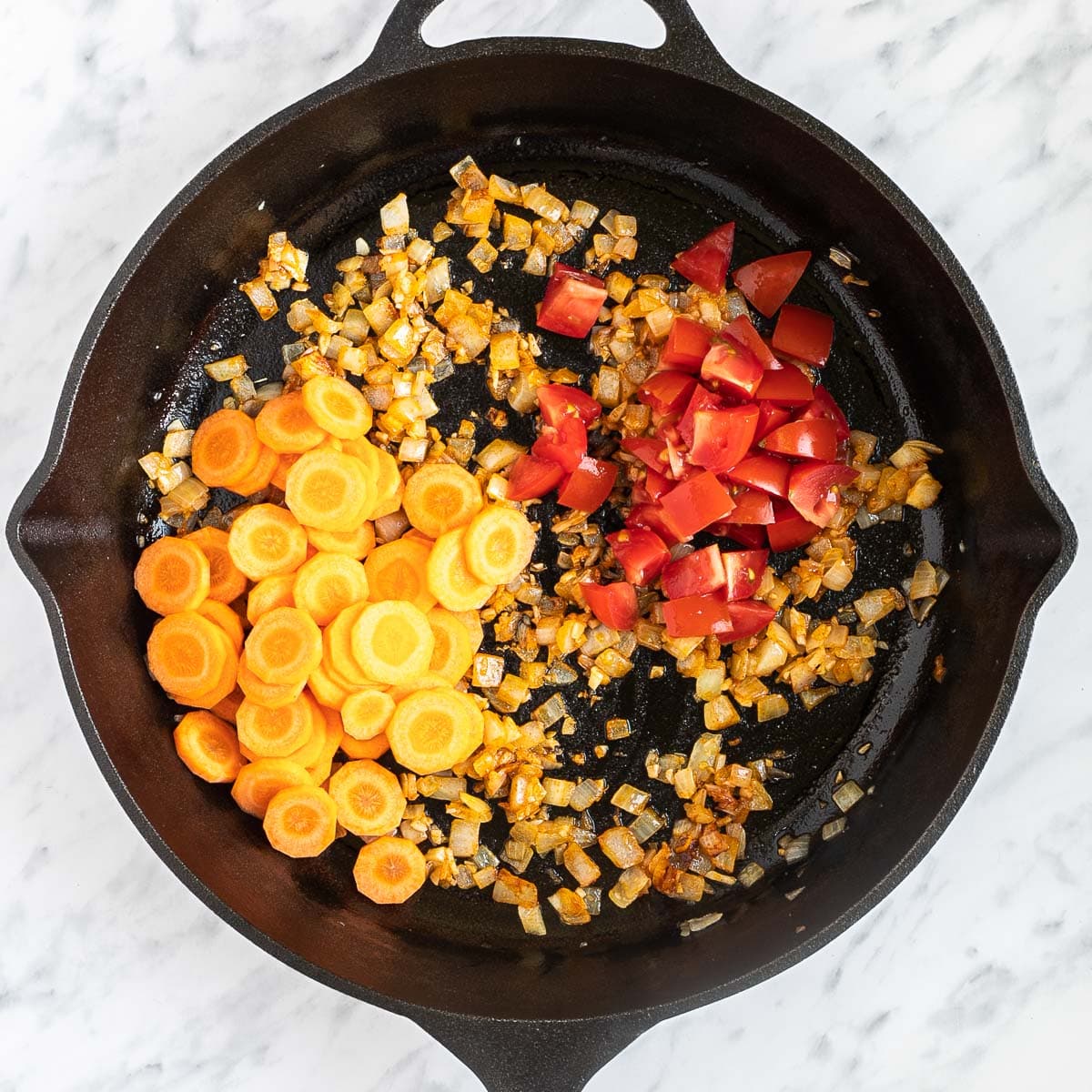 Cast iron skillet with chopped onion, sliced carrots, and chopped red peppers.