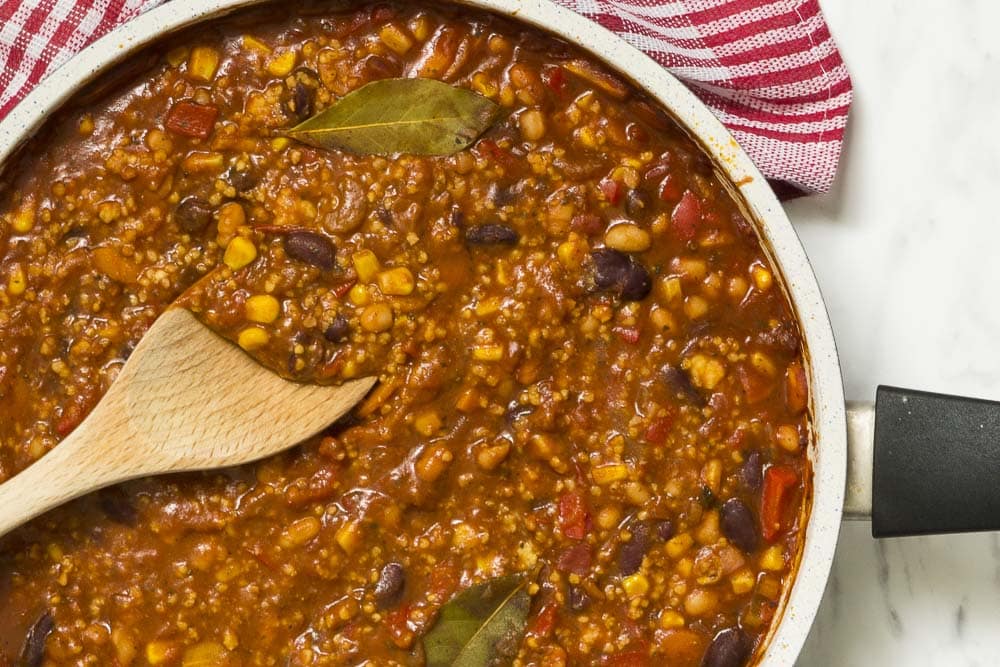 Large frying pan with vegan chili. A wooden spatula is dipped into it. 