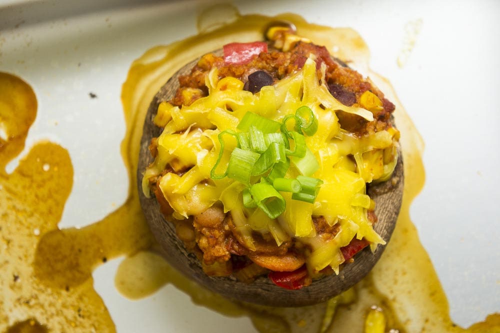 Close-up of a stuffed portobello mushroom on the baking sheet topped with grated cheese and chopped spring onion