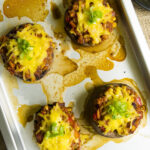 4 mushrooms on a silver baking sheet stuffed with chili topped with melted grated cheese and chopped spring onion