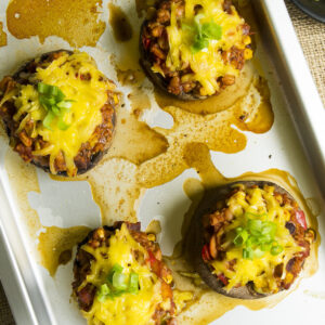 4 mushrooms on a silver baking sheet stuffed with chili topped with melted grated cheese and chopped spring onion