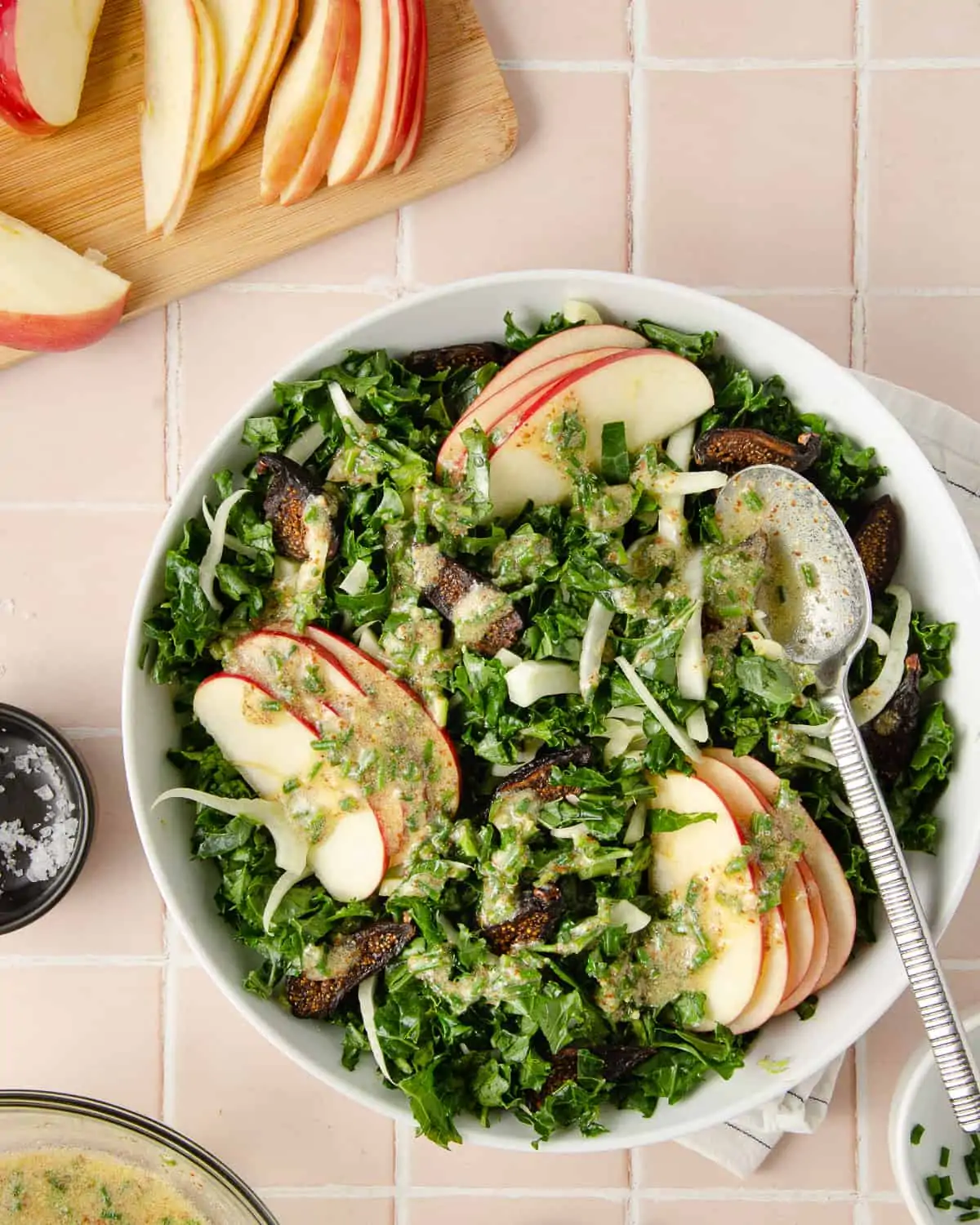 White salad bowl from above with chopped kale, sliced apples, fig halves and a white dressing. 
