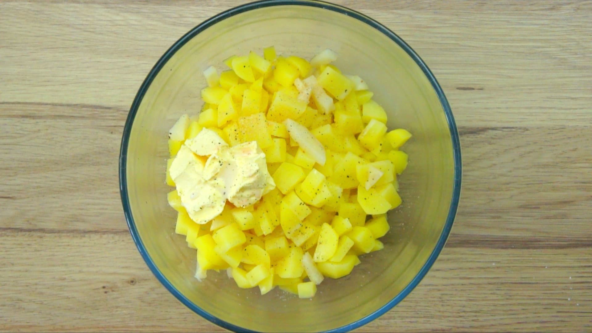 Glass bowl with diced potatoes and scoop of butter.
