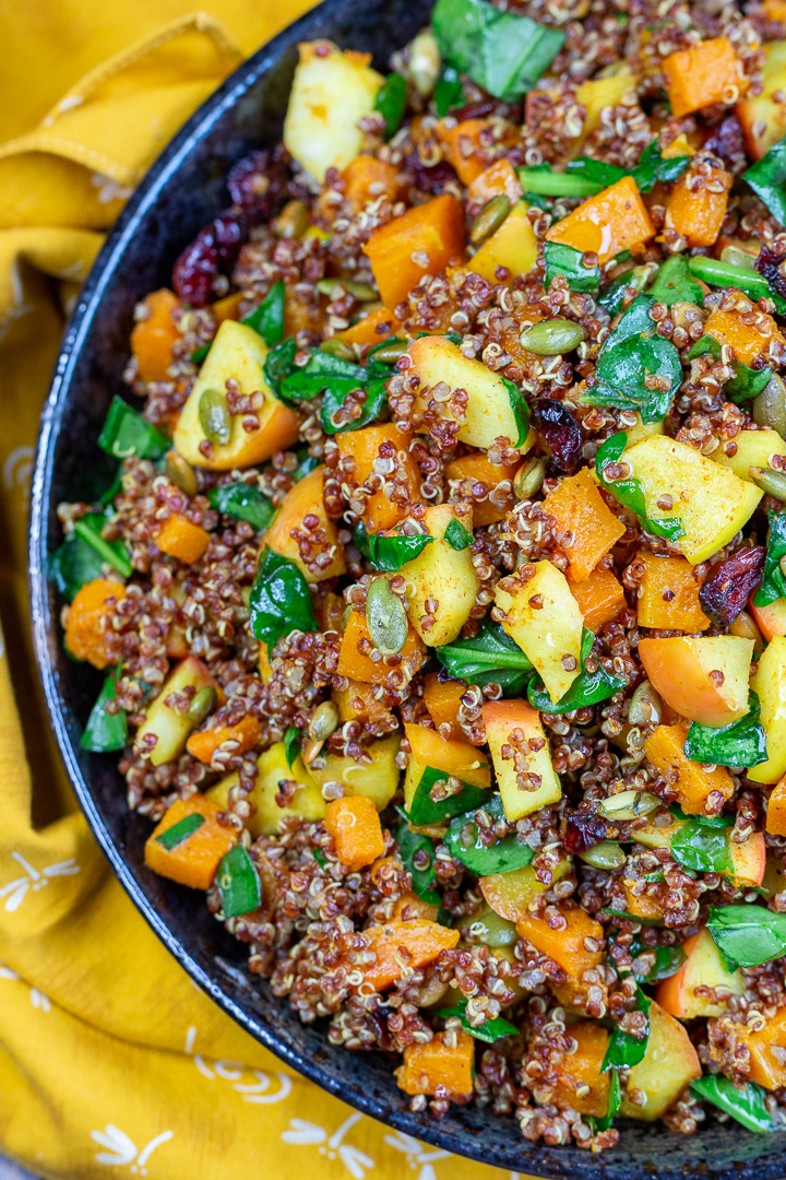 A dark blue salad bowl with chopped apples, diced butternut squash, chopped spinach, pumpkin seeds and brown quinoa