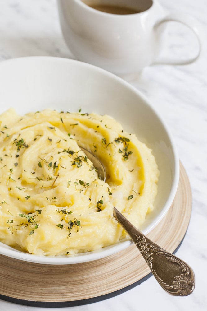 White bowl with yellow mash sprinkled with green herbs. A spoon is placed in the middle. 