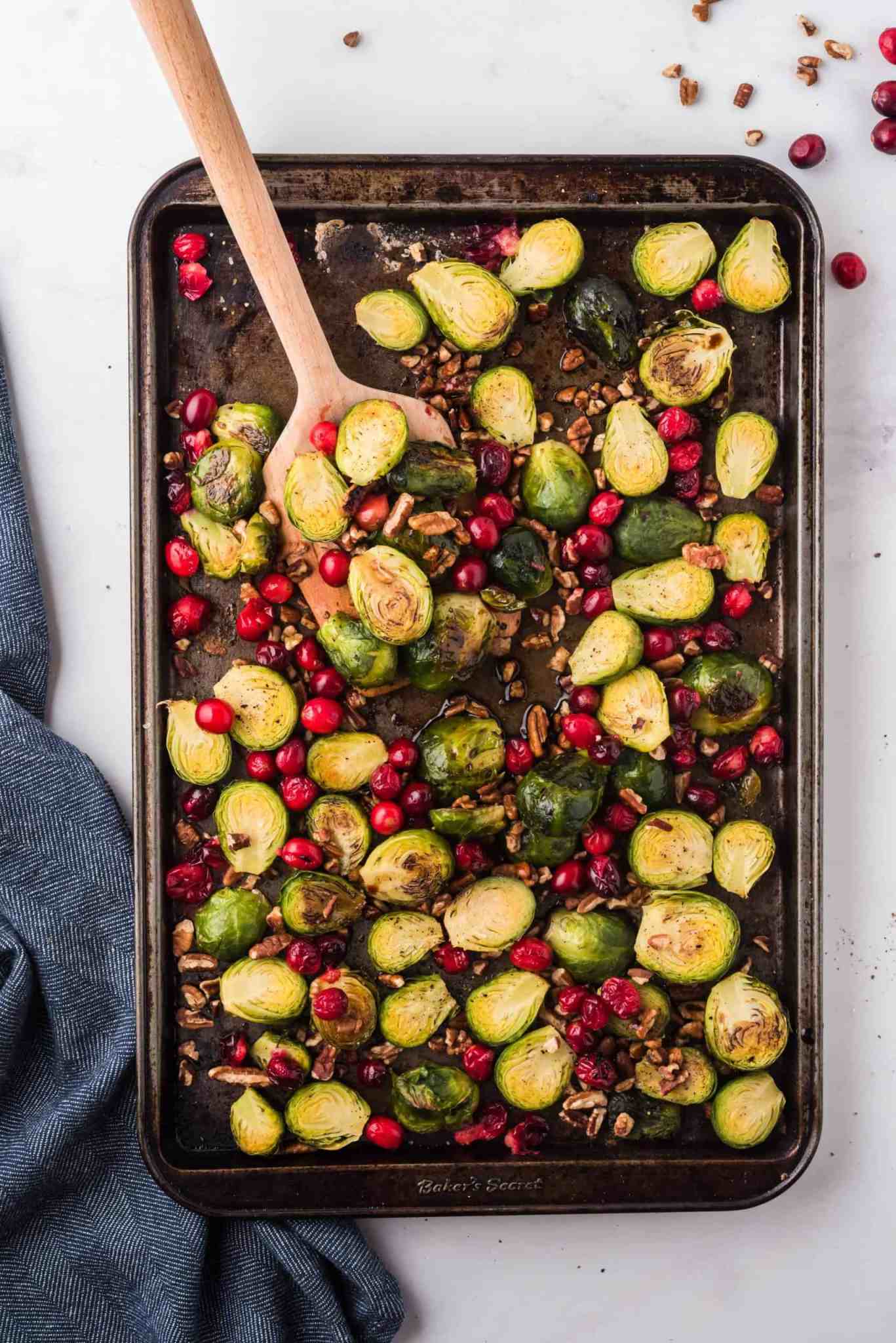 A large baking tray from above with several charred Brussels sprouts halves, pomegranate seeds and chopped nuts
