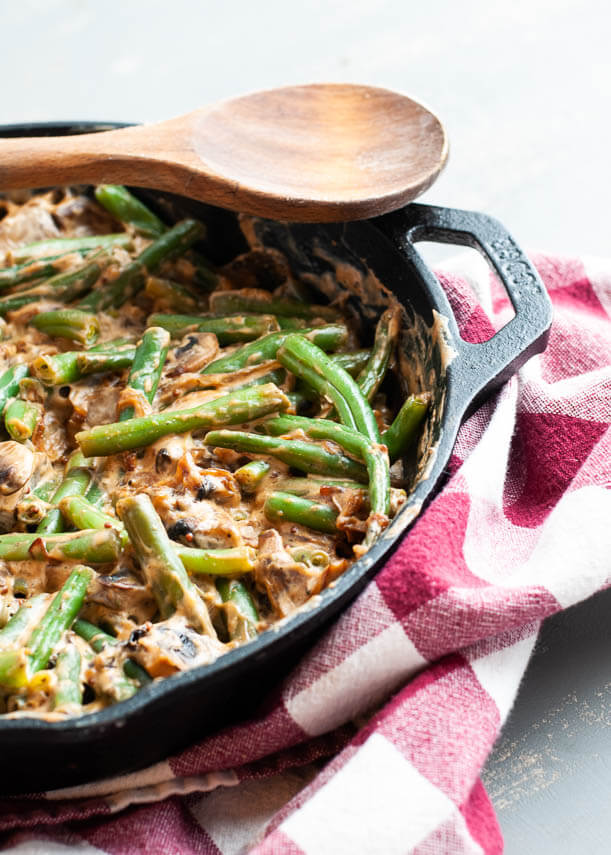 A black cast iron skillet with green beans in a light brown sauce. 