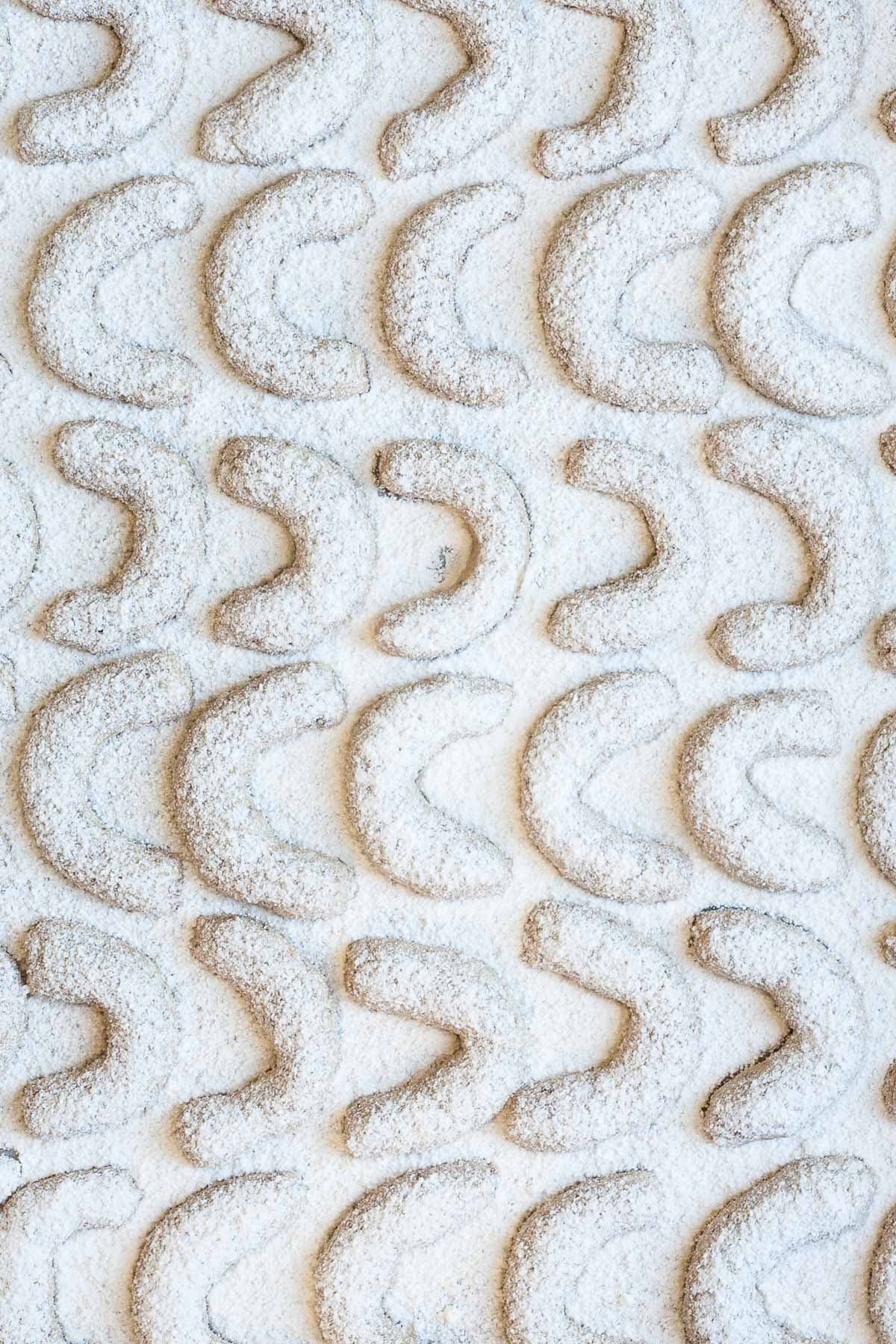 Crescent cookies dusted with powdered sugar on a parchment paper.