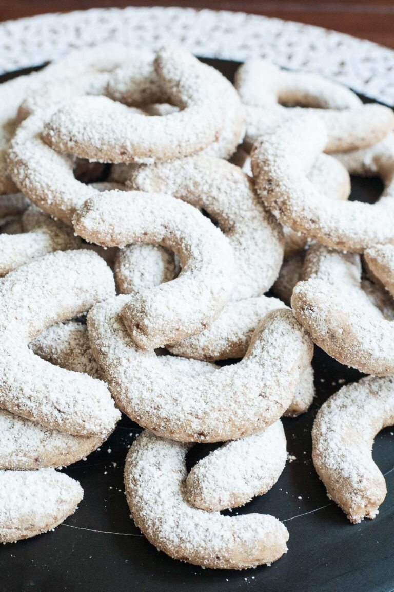 A large stack of crescent cookies on a black plate. Dusted with sugar.