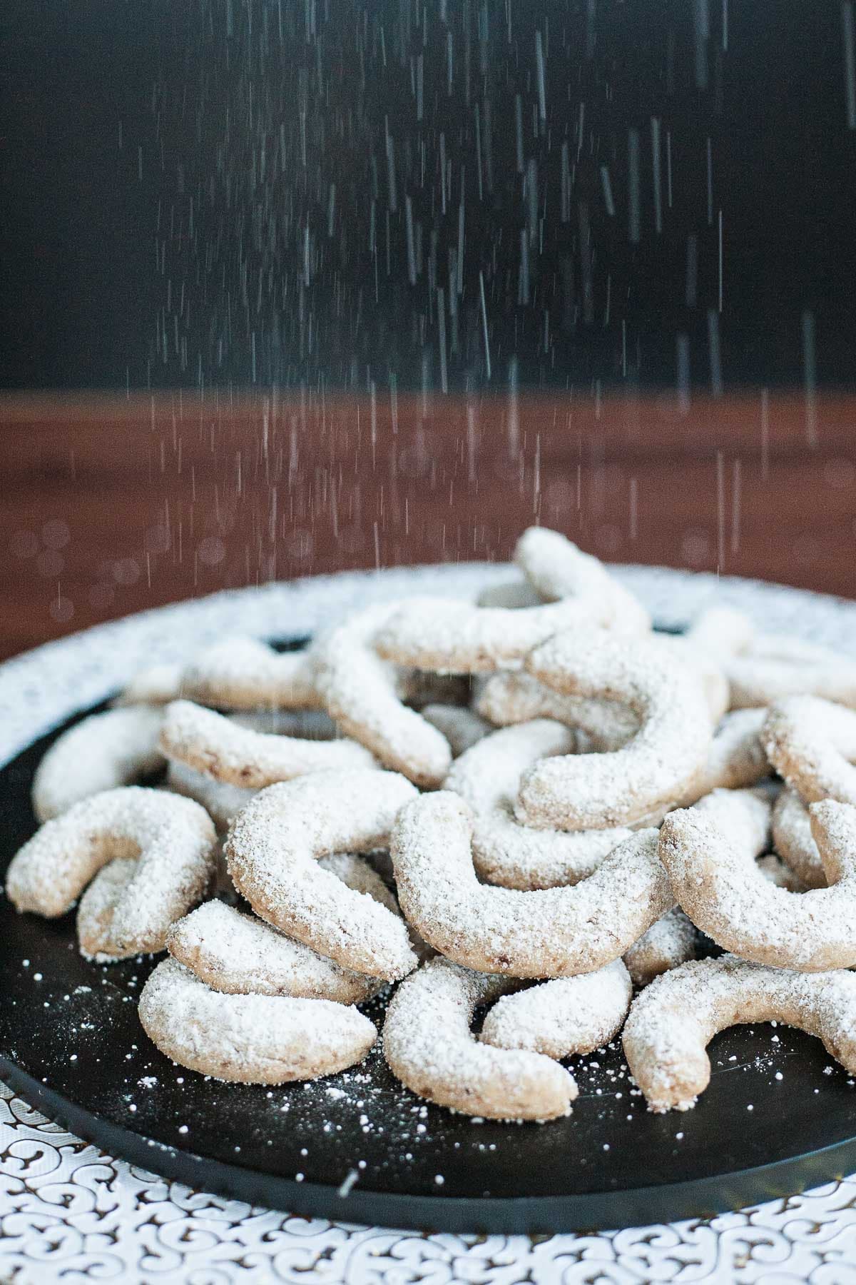 A large stack of crescent cookies on a black plate. Dusted with sugar.