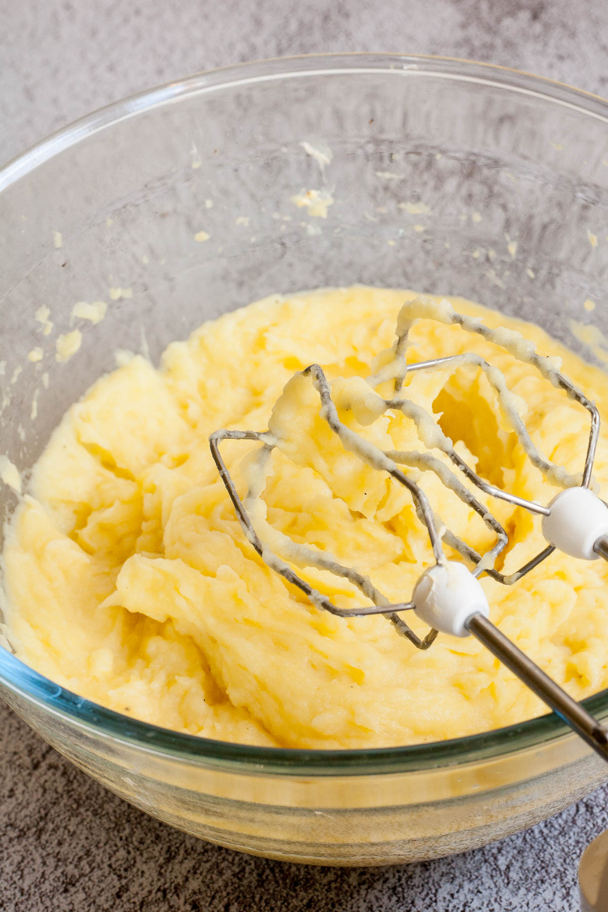 Glass bowl with mashed potatoes and electric whisk.