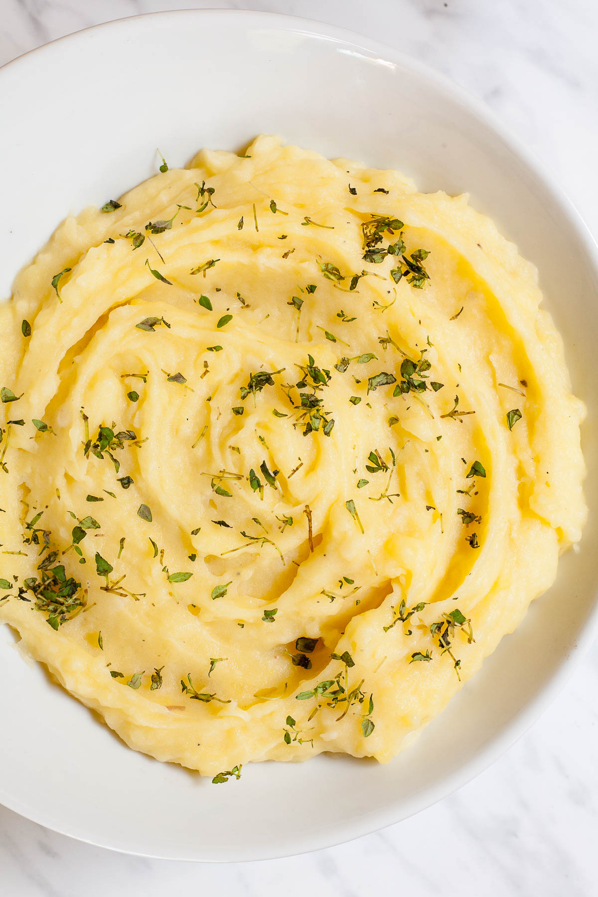 Mashed potatoes sprinkled with green herbs in a white bowl.