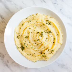 Mashed potatoes sprinkled with green herbs in a white bowl.