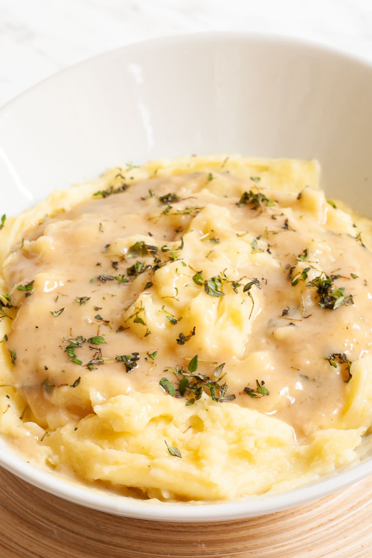 White bowl with mashed potatoes, with light brown gravy and chopped herbs.