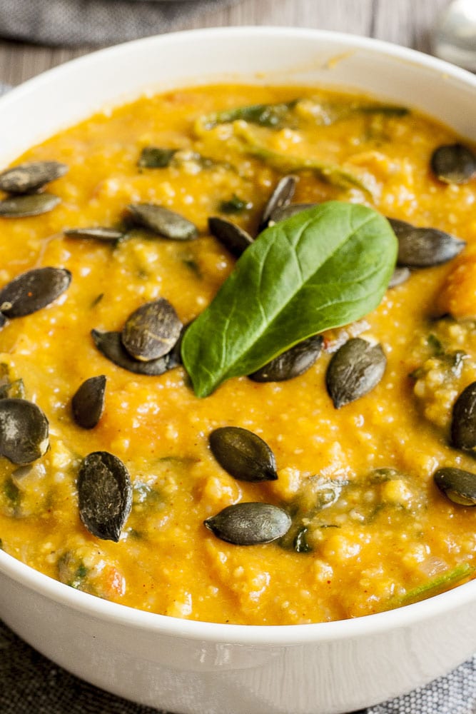 Close-up of vegan sweet potato soup topped with pumpkin seeds and fresh spinach