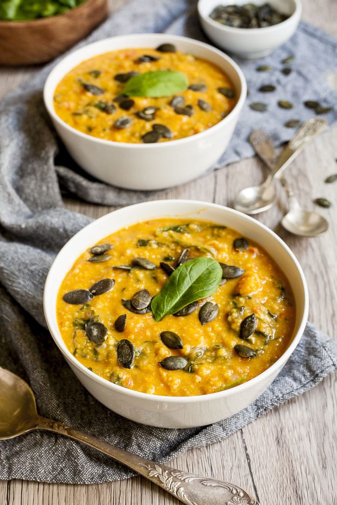 2 white bowl of vegan sweet potato soup topped with pumpkin seeds and fresh spinach