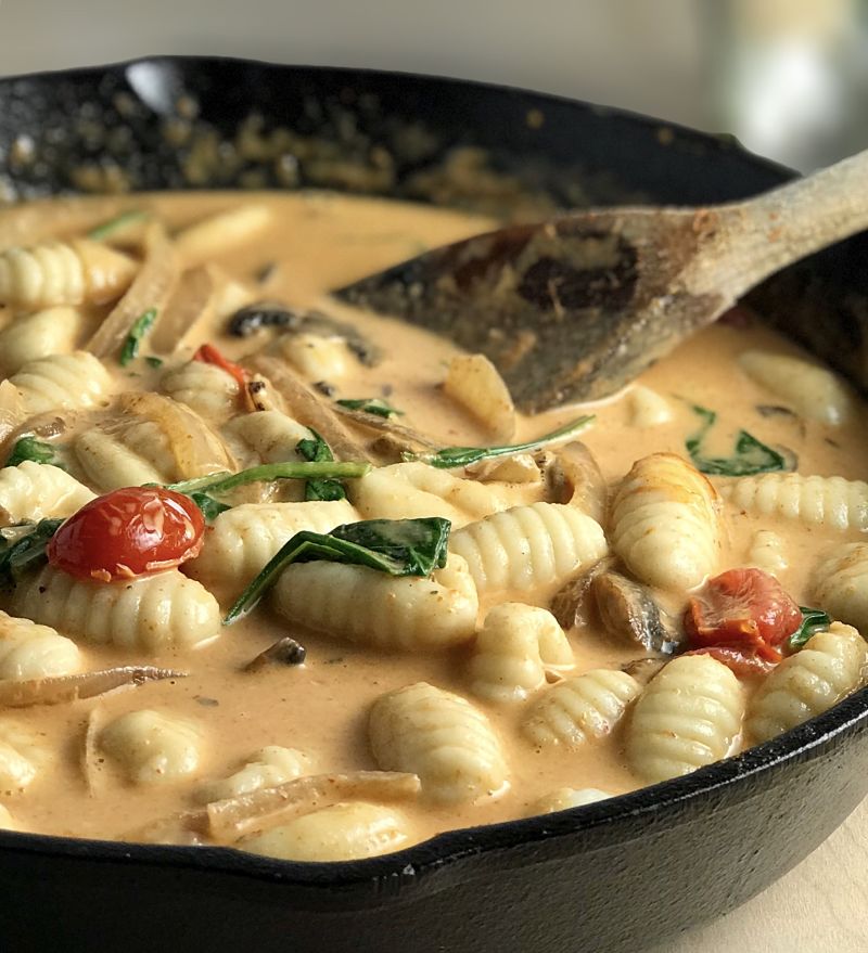 Cast iron skillet with a yellow brown sauce and lots of gnocchi, wilted spinach and cherry tomatoes.