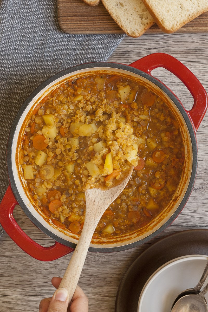 Red Dutch Oven from above with red lentil soup and a wooden spoon