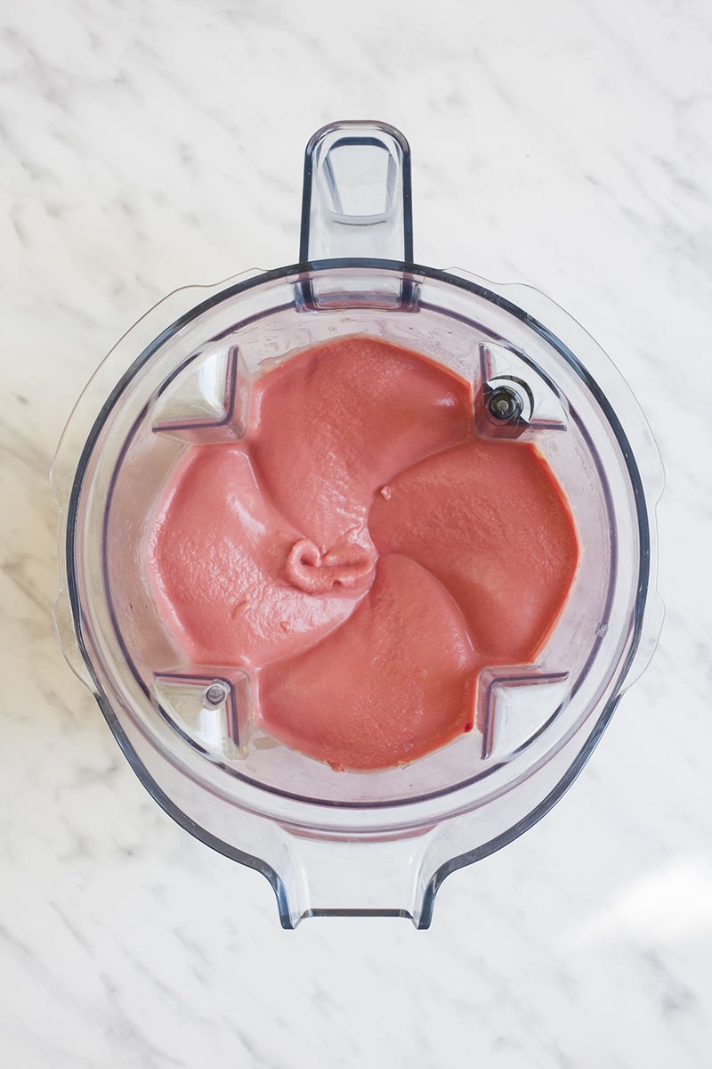 A blender with roasted beet pieces, chickpeas, tahini, lemon juice, garlic clove, and paprika powder.