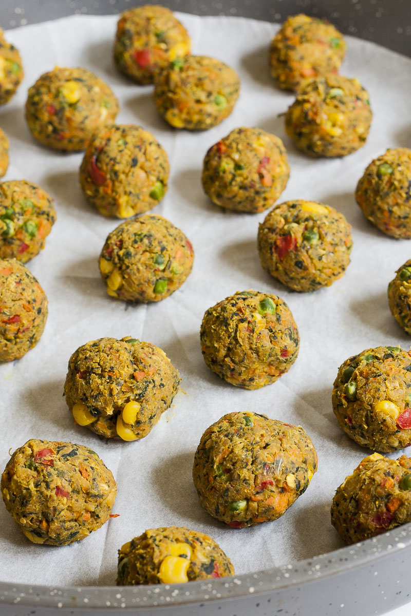 Small brown balls with yellow, red, green pieces on a white parchment paper standing scattered. 