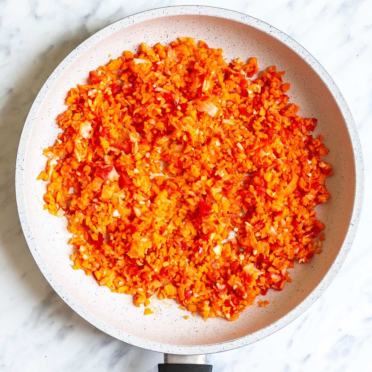 White frying pan with finely chopped carrots, onion, red pepper, and garlic pieces. 