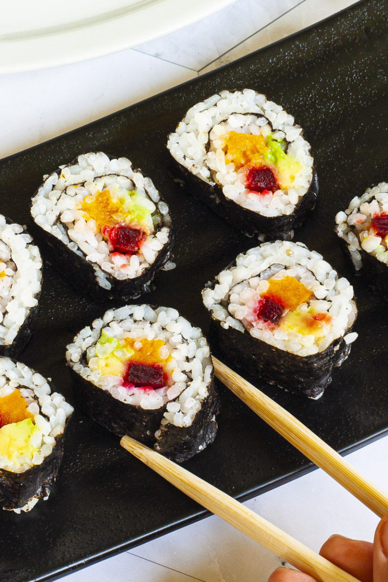 6 sushi rolls on a black plate. The rolls have black cover and white inside with purple yellow and green in the middle.