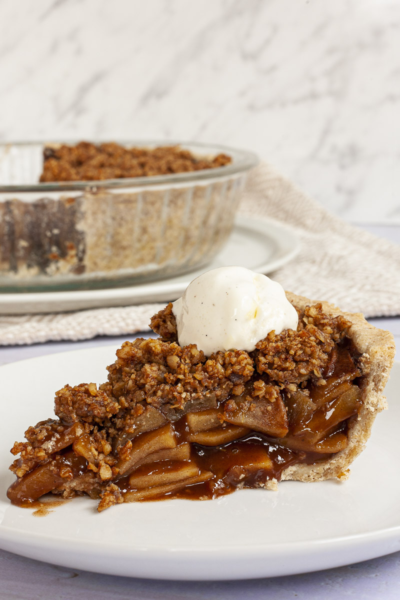 Apple crisp pie on a white plate with vanilla ice cream on top. 