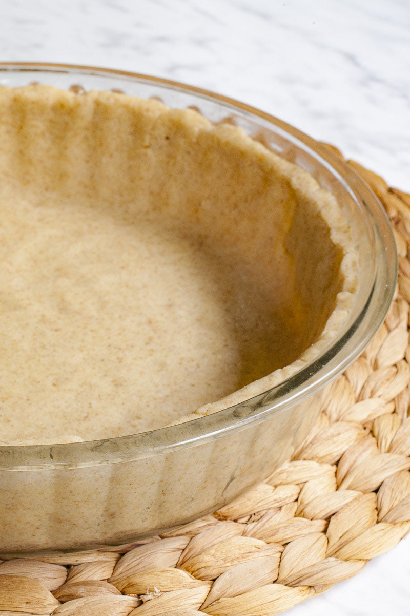 Glass pie pan with brown unbaked pie crust from the side