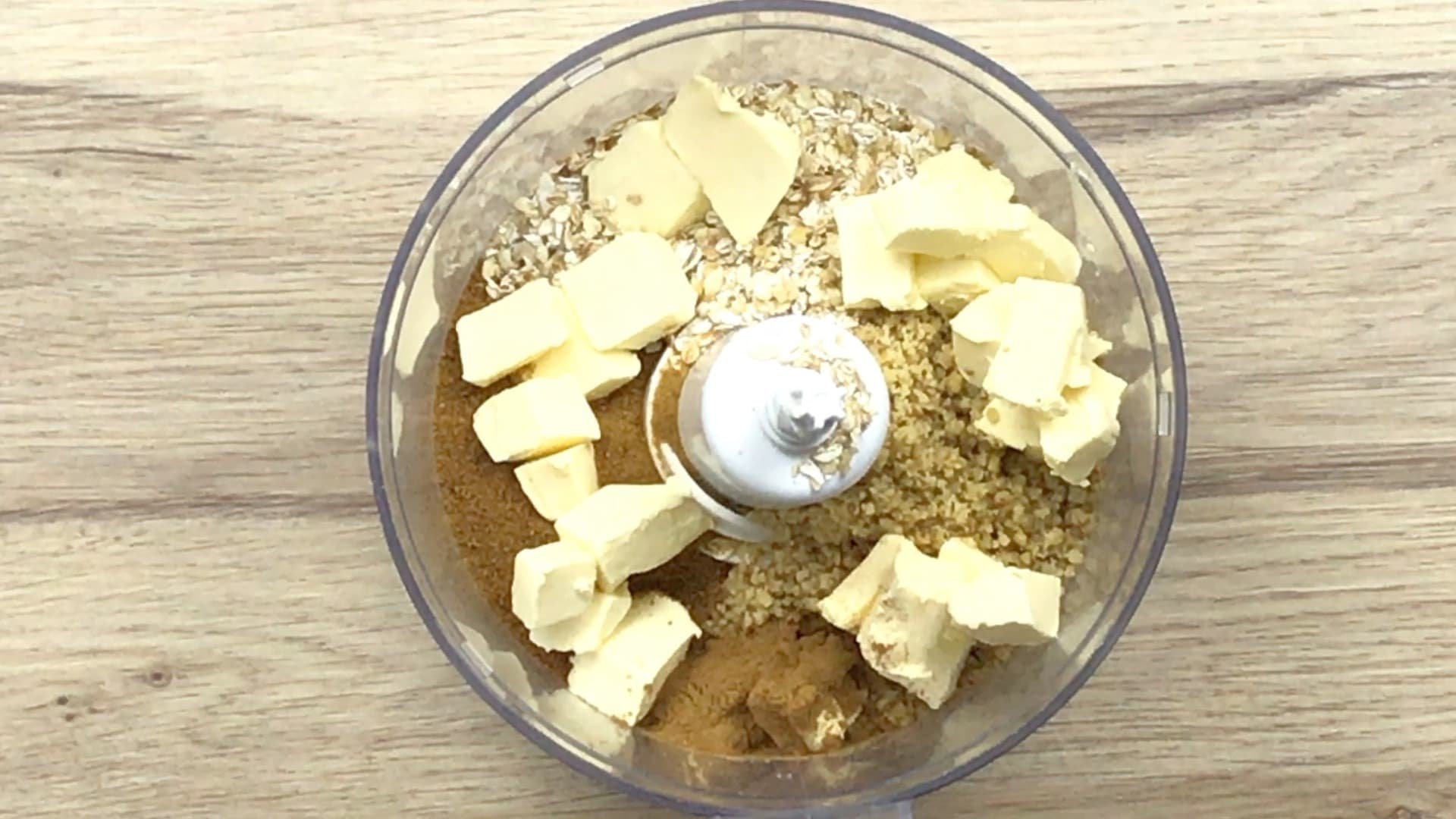 A food processor with oats, butter cubes, and dark sugar. 