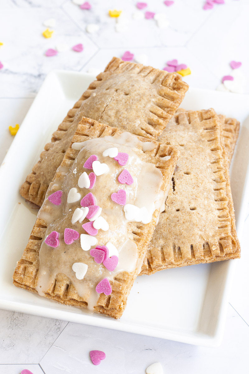 4 pop tarts, rectangle-shaped pillow-like cookies on a white plate. One has white glaze and white and pink small hearts on the top.