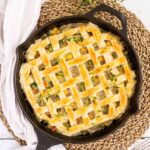 Cast iron skillet with veggie stew topped with puff pastry in a lattice pattern.