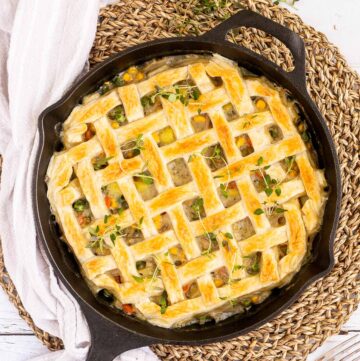 Cast iron skillet with veggie stew topped with puff pastry in a lattice pattern.